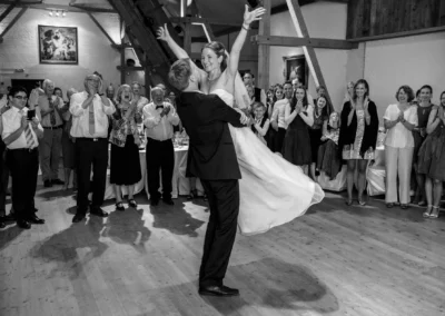 Brautpaar tanzt bei Hochzeitsfeier in Gut Georgenberg, umgeben von applaudierenden Gaesten in einer rustikalen Halle.