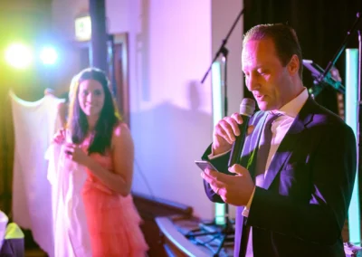 Mann haelt Rede bei Hochzeit im Gasthof Widmann, Frau in rosa Kleid hoert zu. Hochzeitsreportage aus Gilching.