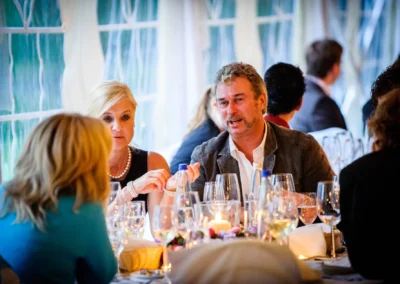 Ein Mann und eine Frau sitzen an einem gedeckten Tisch, umgeben von Gläsern und Kerzenlicht, im Gespräch vertieft.