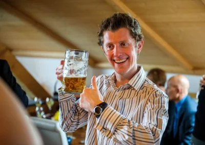 Ein Gast hebt einen Bierkrug und lacht bei einer Hochzeit in Dietramszell. Hochzeitsreportage in Oberbayern.