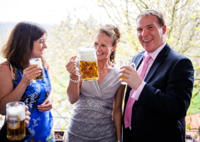 Gäste bei einer Hochzeit im Moarwirt Hechenberg stoßen mit Bierkrügen an. Hochzeitsfoto in fröhlicher Stimmung.