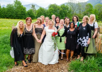 Braut mit Freundinnen auf Hochzeit in Kreuth am Tegernsee, lachend in bunter Gruppe, umgeben von gruenem Feld.