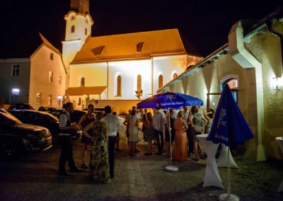 Gaste bei einer Hochzeit nahe Starnberger See, aufgenommen vom Hochzeitsfotografen. Feier vor einer erleuchteten Kirche.