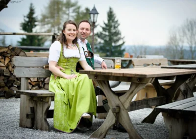 Brautpaar in Tracht sitzt an Holztisch im Freien, Hochzeitsfoto aufgenommen am Moarwirt Hechenberg.