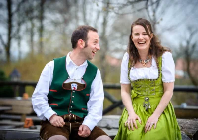 Brautpaar in traditioneller Tracht lacht bei Bio Landhotel Moarwirt. Hochzeitsfoto aus Hechenberg, Oberbayern.