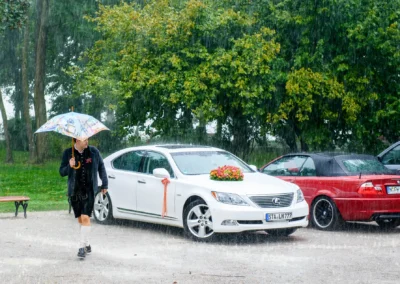 Mann mit Regenschirm steht bei Hochzeitsauto im Regen, standesamtliche Trauung in Herrsching am Ammersee.