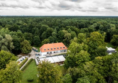 Luftaufnahme der Hochzeitslocation im Waldhaus Alte Tram Strasslach, umgeben von dichtem Gruen.