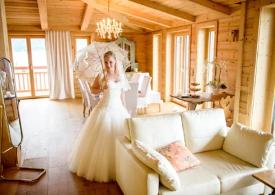 Braut posiert im Holzraum mit elegantem Kleid und Schirm, Hochzeitsfotografie bei Tegernsee.