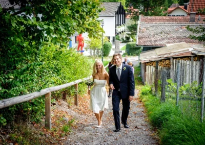 Paar auf Weg zur standesamtlichen Trauung in Bernried am See. Grüne Natur und historische Gebäude im Hintergrund. Hochzeitsfoto.