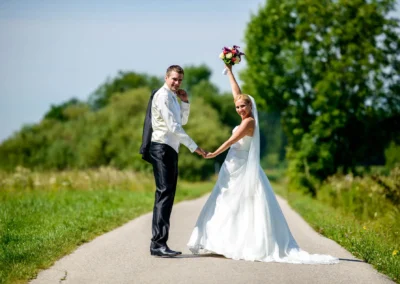 Brautpaar posiert auf Landstrasse nahe Muenchen, Braut hebt Blumenstrauss, Hochzeitsportrait von Hochzeitsfotograf.
