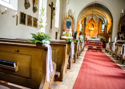 Kirchliche Trauung in Pasing mit dekorierten Baenken und Altar im Hintergrund. Hochzeitsfotografie in einer Kirche.