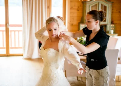 Braut bei Hochzeitsvorbereitung in Tegernsee, hilft mit Kleid. Hochzeitsreportage von Hochzeitsfotograf.