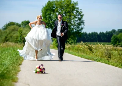 Brautpaar laeuft auf Landstrasse nahe Muenchen; Hochzeitsfoto in natuerlicher Umgebung.