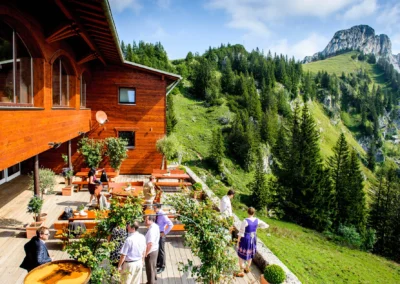 Hochzeitsgesellschaft auf Terrasse neben Holzhaus mit Alpenblick bei der Kampenwand in Oberbayern. Hochzeit Reportage.
