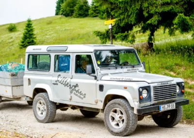 Geländewagen mit Anhänger auf Schotterweg bei Berg-Hochzeit am Sillberghaus in Oberbayern, umgeben von grünen Bäumen.