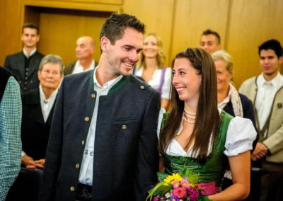 Brautpaar bei standesamtlicher Trauung in Muenchen, lächelnd in traditioneller Kleidung mit Blumenstrauss.