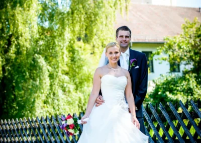 Brautpaar in Taufkirchen nahe Muenchen vor einer Kirche, beide laechelnd, Braut in weissem Kleid mit Blumenstrauss.