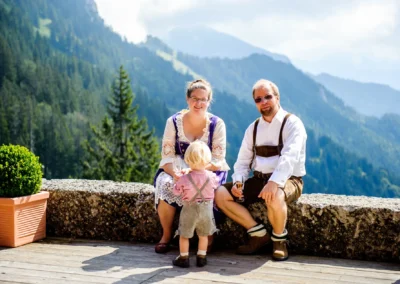 Familie in traditioneller bayerischer Kleidung auf einer Terrasse, umgeben von Bergen bei der Kampenwand Hochzeit.