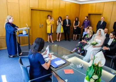 Standesamtliche Trauung in München Schwabing. Brautpaar sitzt neben Trauzeugen, umgeben von Gästen. Hochzeitsfotografie.