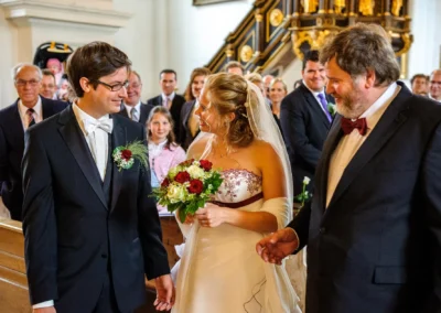 Brautpaar bei kirchlicher Trauung im Kloster Benediktbeuern, fröhliche Gäste im Hintergrund, Hochzeitsreportage.