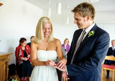 Braut steckt Bräutigam in Bernried am See beim Standesamt den Ring an den Finger, umgeben von Hochzeitsgästen.