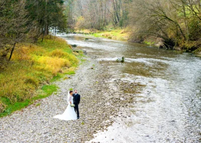 Brautpaar am Flussufer bei der Mangfall, umgeben von herbstlichen Baumen, festgehalten in einem Hochzeitsfoto.