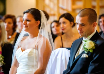 Brautpaar bei kirchlicher Trauung in Murnau, lächelnd im Hochzeitssaal mit Gästen im Hintergrund. Hochzeitsfotografie.