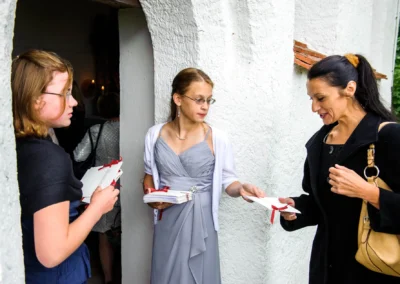 Frauen verteilen Hochzeitsprogramme bei einer kirchlichen Trauung in einer Kapelle auf Gut Thurnsberg.