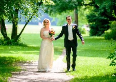 Brautpaar geht Hand in Hand durch einen grünen Park in München bei ihrer Hochzeitsfotografie im Sommer.