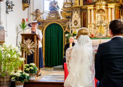 Kirchliche Trauung in Sankt Martin Waakirchen. Frau spricht am Rednerpult, Brautpaar im Vordergrund, goldener Altar.