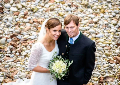 Brautpaar bei Hochzeitsfoto an Kieselsteinen in Mangfall, Brauttraeger in Tracht. Hochzeitsfotografie Muenchen.
