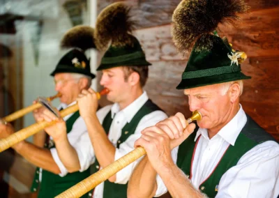 Musiker in traditioneller Tracht spielen Alphorn bei Hochzeit im Chiemgau, festgehalten von Hochzeitsfotografie.