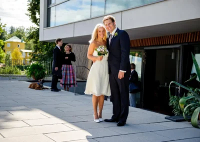 Brautpaar bei der standesamtlichen Trauung in Bernried, Paar laechelt vor moderner Architektur. Hochzeitsszene.