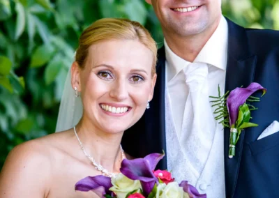 Brautpaar laechelt in die Kamera bei Hochzeitsfotos in Taufkirchen. Farbenfrohes Blumenbouquet im Vordergrund.