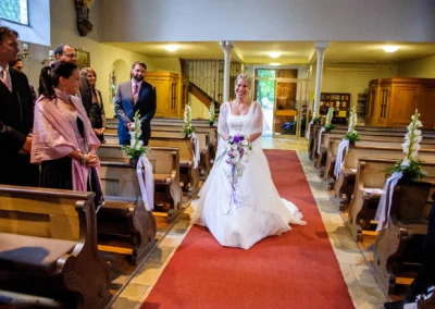 Braut schreitet den Gang der Kirche entlang zur Hochzeit in Pasing, begleitet von Gästen und Blumendekorationen.