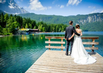 Brautpaar auf Steg am Eibsee bei Garmisch, Hochzeit aufgenommen von Hochzeitsfotograf bei sonnigem Wetter und Bergkulisse.