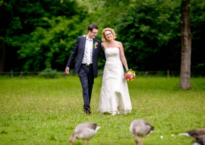 Brautpaar spaziert im Englischen Garten Muenchen, umgeben von Gruen und Gaensen. Hochzeitsfotografie in natuerlicher Umgebung.
