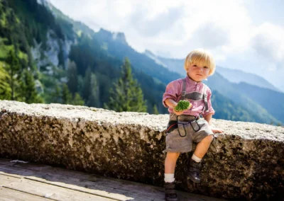 Kleinkind in Tracht nahe des Chiemsees, im Hintergrund Berge und Wald, Hochzeitsfotografie in Oberbayern.