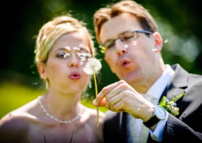 Brautpaar pustet Pusteblume bei Hochzeitsfoto im Kloster Seeon, Chiemgau. Hochzeitsfotografie in Oberbayern.