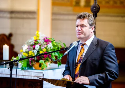 Mann am Mikrofon bei kirchlicher Trauung in evangelische Friedenskirche, Starnberger See, blumige Dekoration.