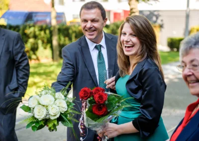 Lachende Hochzeitsgaeste mit Blumenstraeussen bei der standesamtlichen Trauung in Pasing. Hochzeitsfoto von München.