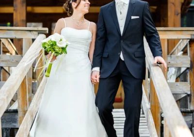 Brautpaar bei Hochzeit am Eibsee, laechelnd auf Holzbruecke gehend, Hochzeitsfoto von Hochzeitsreportage.