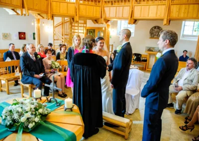 Kirchliche Trauung in Murnau: Brautpaar vor Altar, Gaeste auf Baenken, Blumenschmuck und Kerzen im Vordergrund.