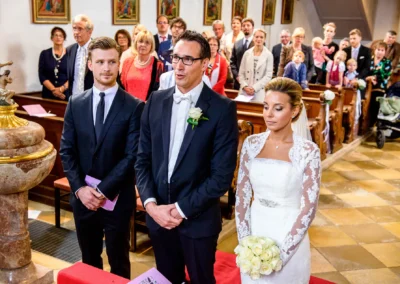 Brautpaar bei kirchlicher Trauung in Waakirchen, umgeben von Hochzeitsgaesten in der Kirche. Hochzeitsreportage.