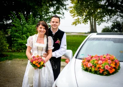 Brautpaar vor mit Blumen geschmuecktem Wagen am Standesamt Herrsching, Hochzeitsfoto im Freien, Hochzeitstag.