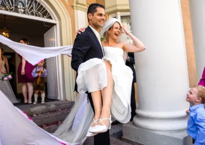 Brautpaar verlässt standesamt Mandlstrasse, der Bräutigam trägt die Braut, Hochzeit in München Schwabing.