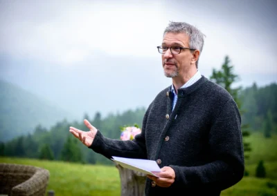 Mann in grauem Trachtenjanker spricht bei freier Trauung in Almbad-Sillberghaus, umgeben von Berglandschaft.