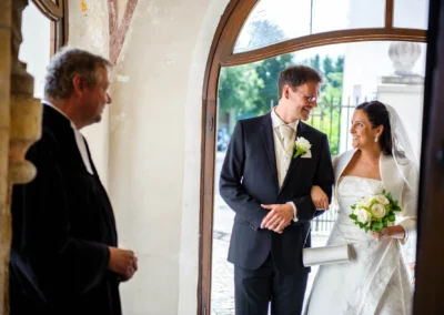 Brautpaar laechelt am Kircheneingang in Aufkirchen, Oberbayern. Hochzeitsfoto von kirchlicher Trauung.