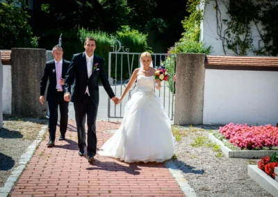 Brautpaar bei kirchlicher Trauung in Taufkirchen. Braut im weissen Kleid, Bräutigam im Anzug, begleitet von Gast.