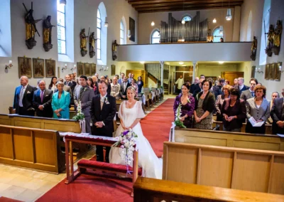Kirchliche Trauung in Pasing. Brautpaar und Gaeste in der Kirche waehrend der Hochzeitszeremonie. Hochzeitsfoto aus Muenchen.